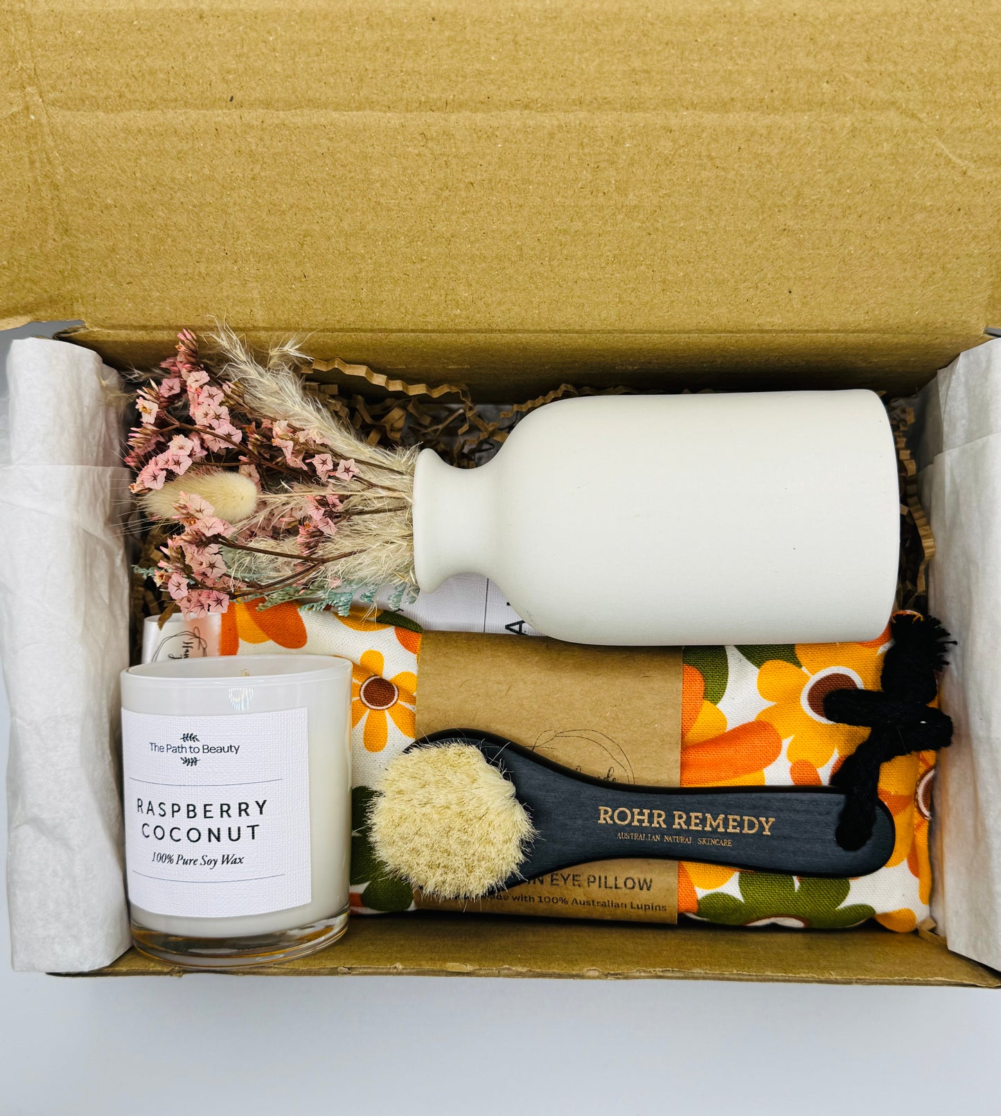Box containing a candle, bottle, brush, and other items with visible branding.