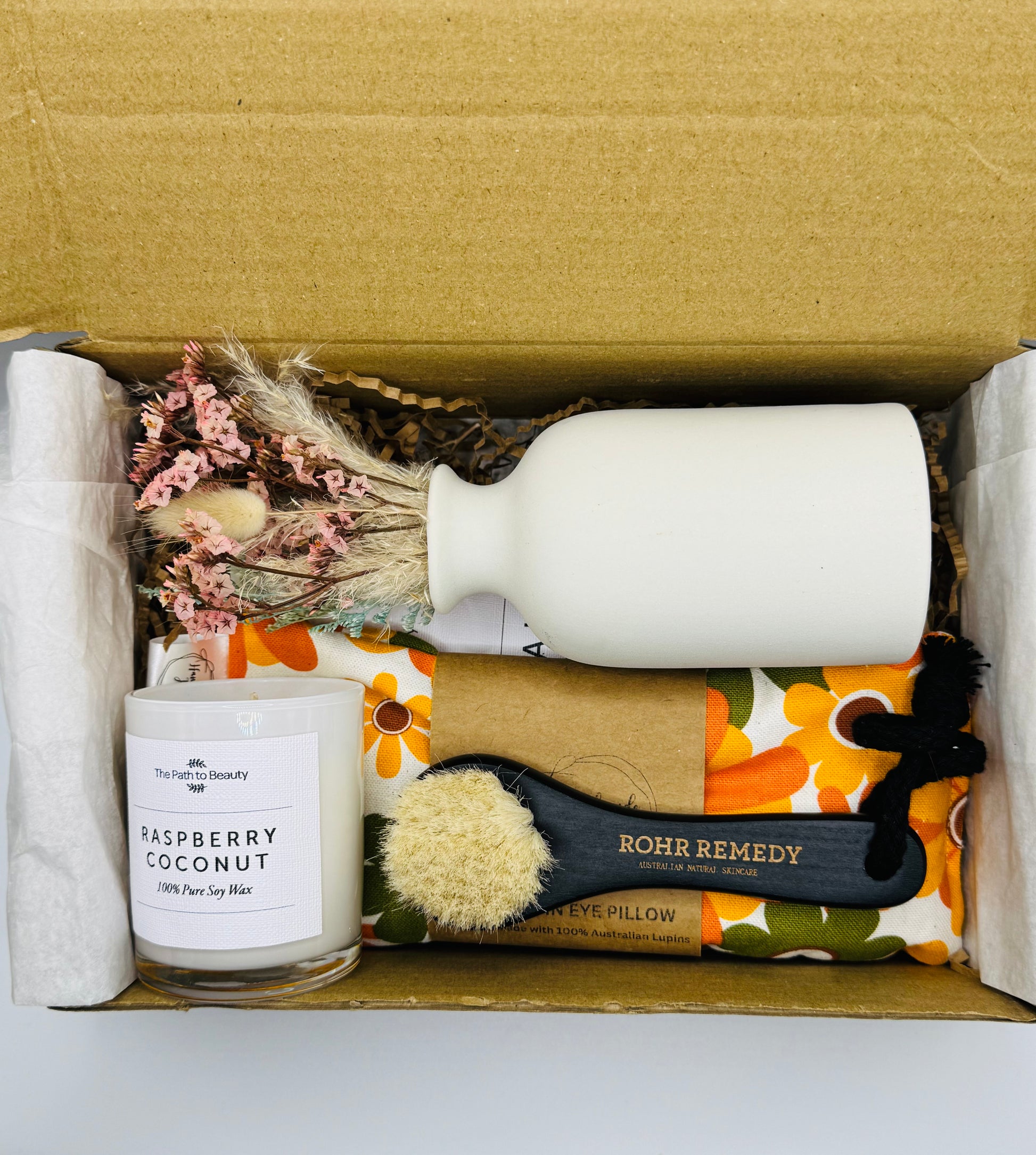 Box containing a candle, bottle, brush, and other items with visible branding.